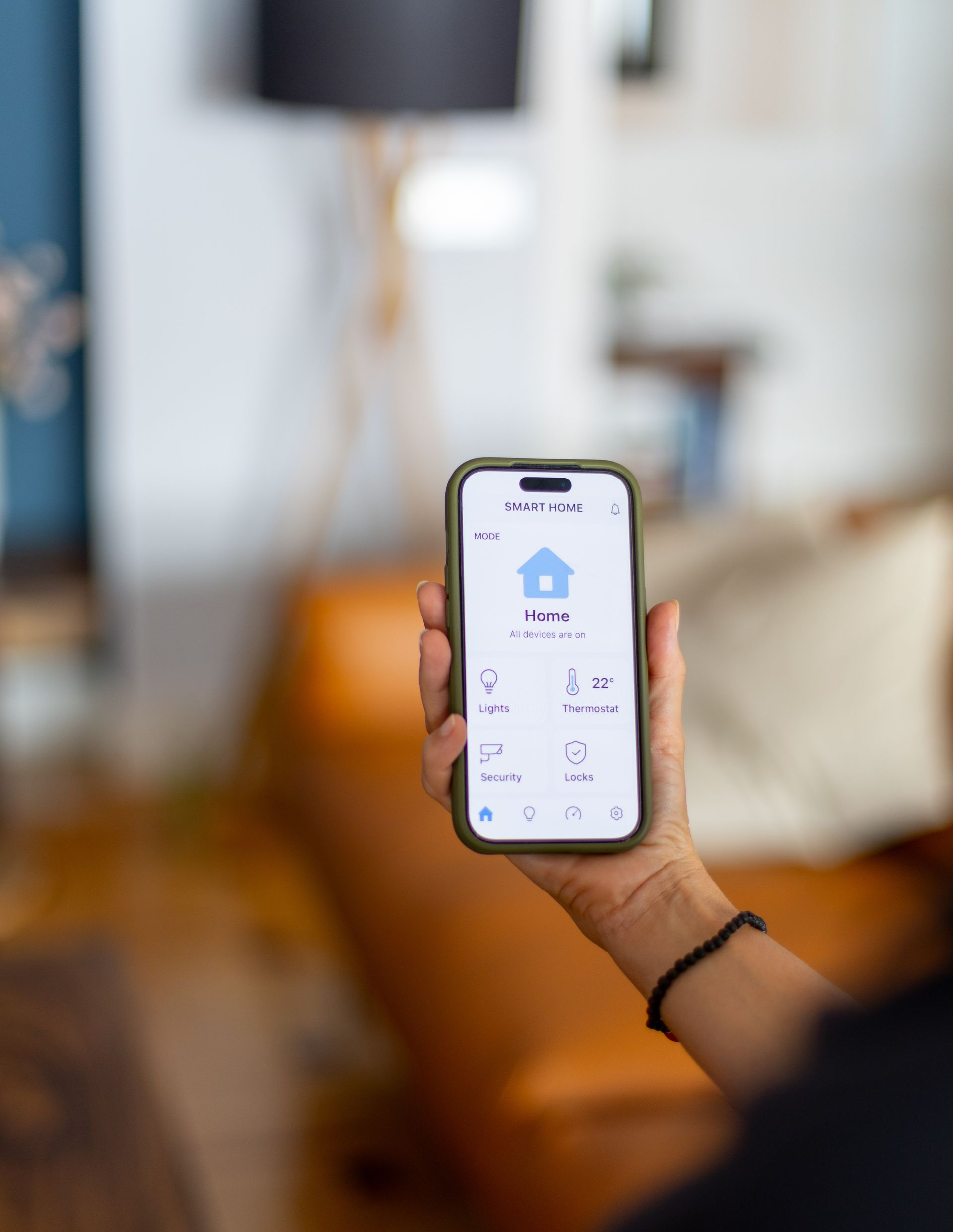 Une personne tient un smartphone affichant une application de contrôle domotique. Intérieur avec canapé.