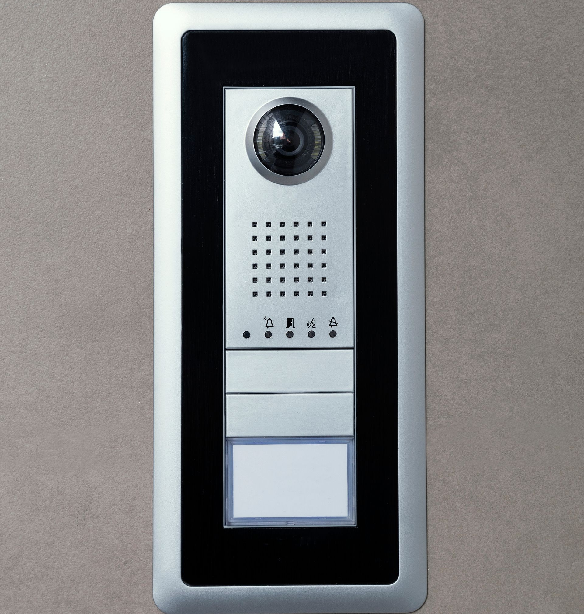 Sonnette vidéo fixée sur un mur, comprenant une caméra, un haut-parleur et une plaque nominative.