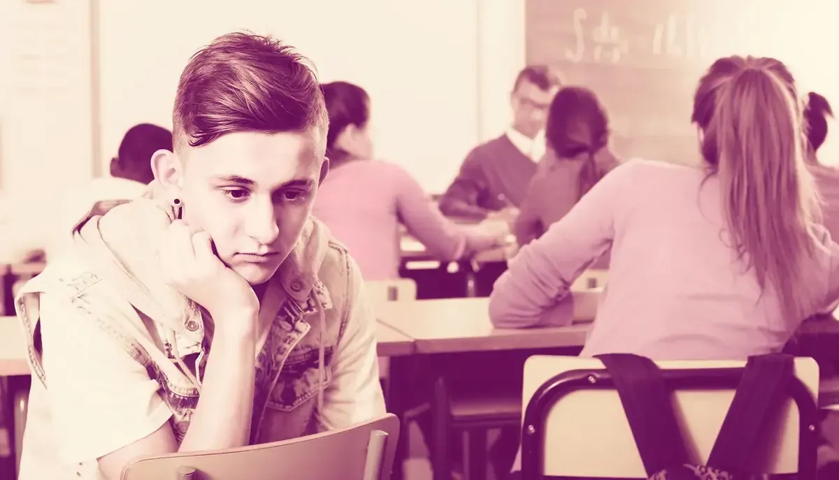 Un adolescente abatido se sienta solo en un pupitre en un aula, con la mirada baja