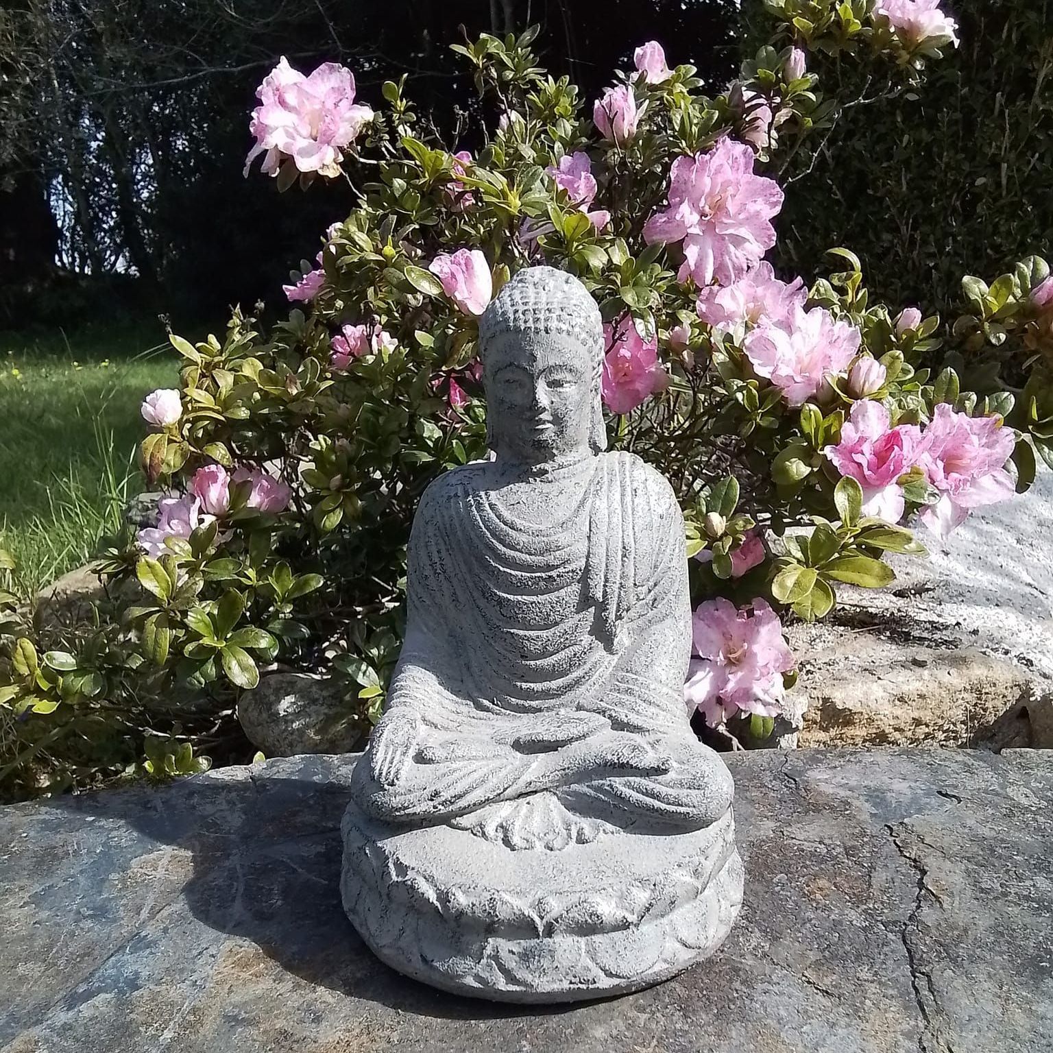 Une statuette en pierre de bouddha devant des fleurs