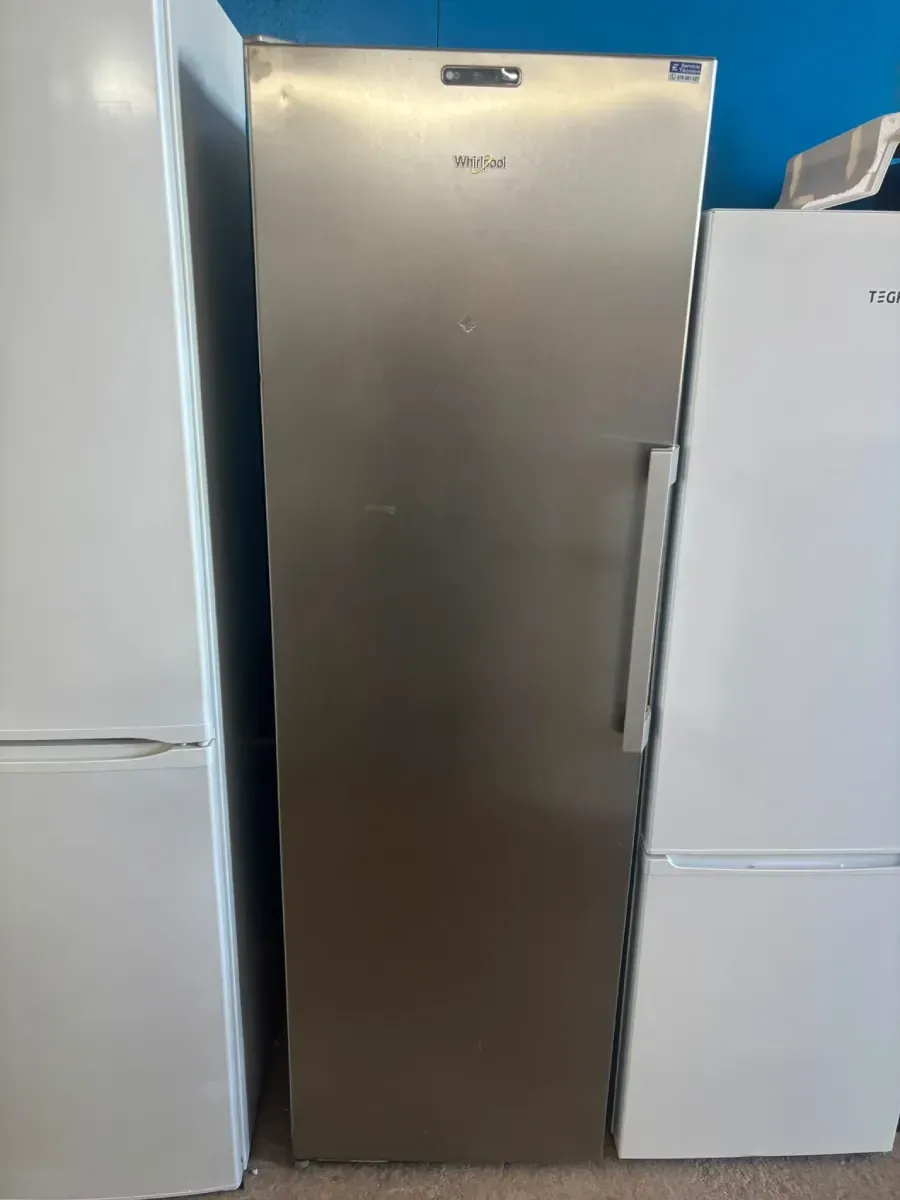 Un frigorífico alto de acero inoxidable se encuentra entre dos frigoríficos blancos en el pasillo de una tienda.