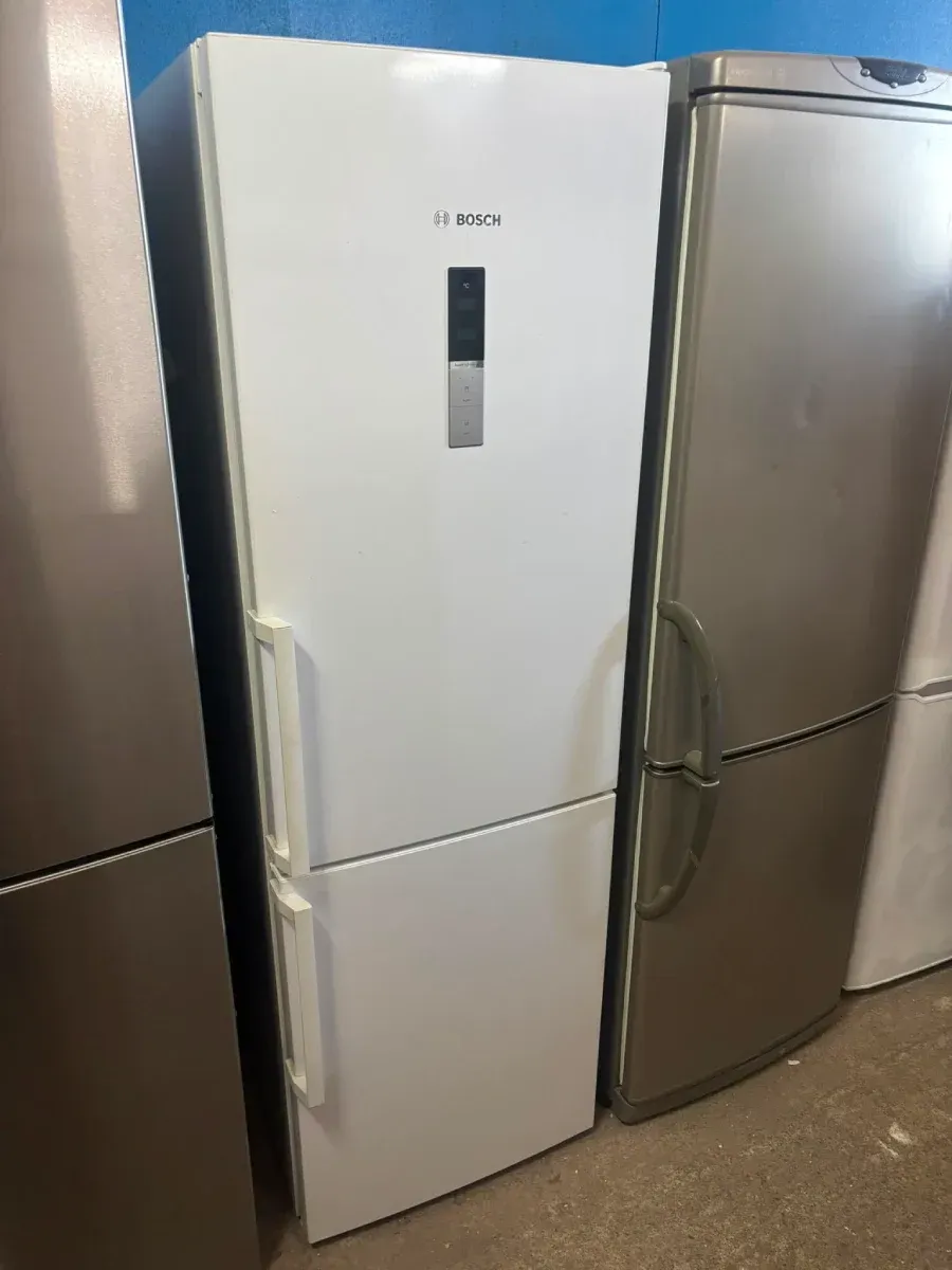 Refrigerador vertical blanco entre dos refrigeradores de acero inoxidable en una exposición de cocinas.