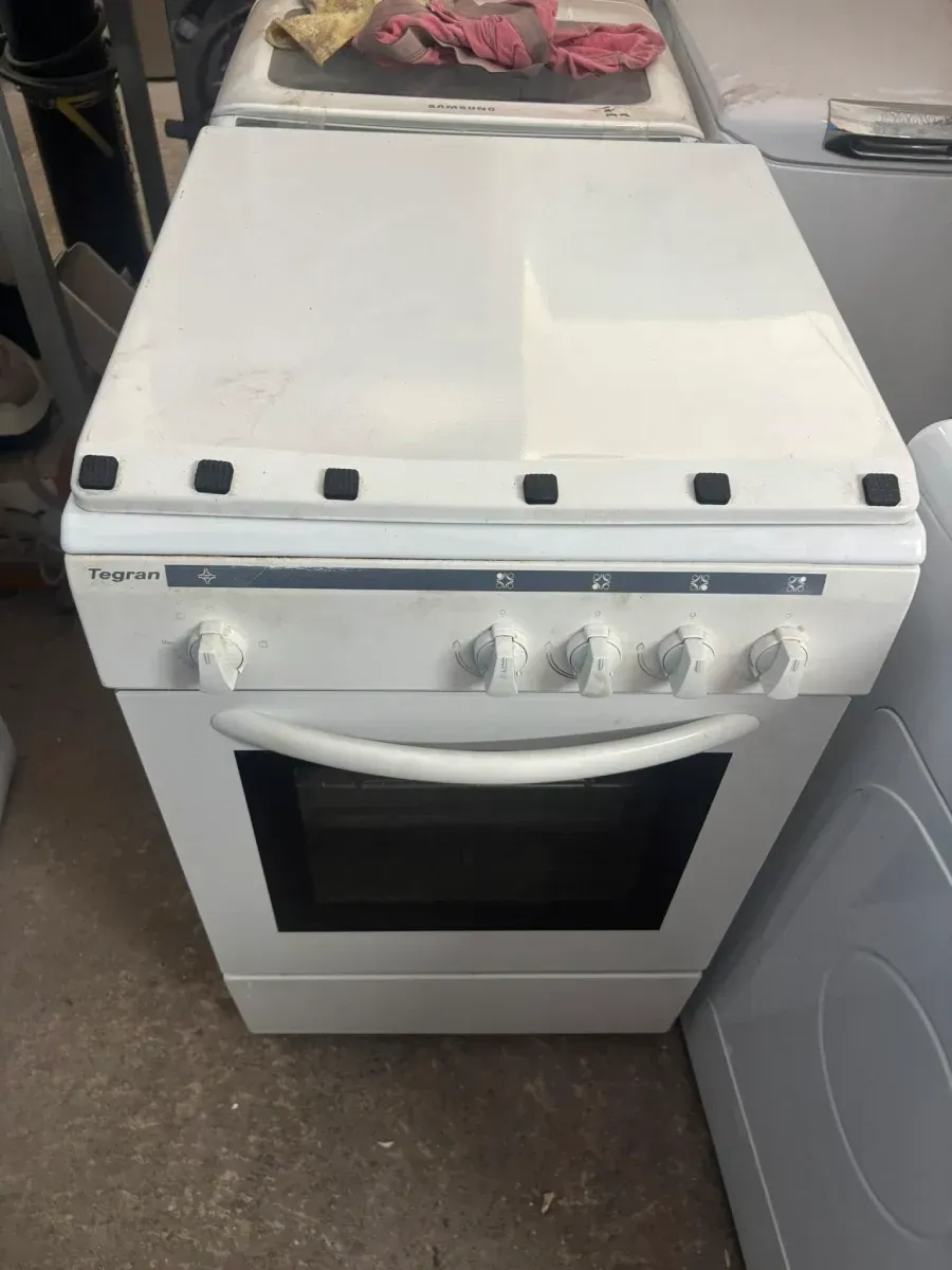 Cocina/horno independiente de color blanco con cuatro quemadores y mandos de control en una zona de cocina/lavadero.