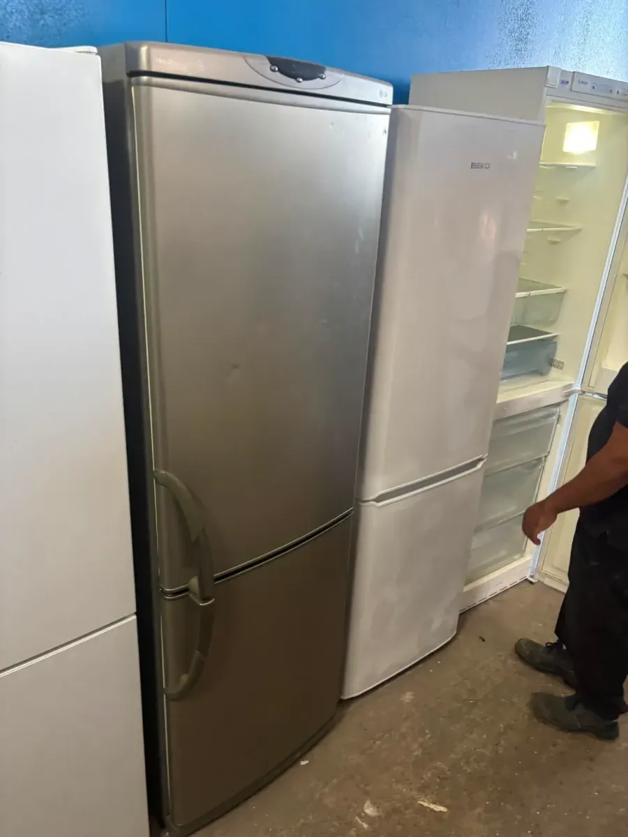 Nevera de acero inoxidable al lado de una nevera blanca, con una vitrina refrigerada abierta y una persona de pie cerca.