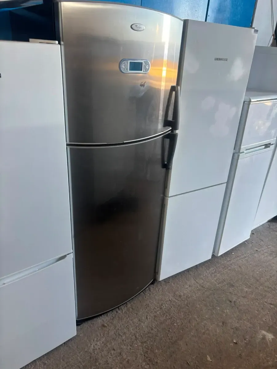 Tres refrigeradores verticales en una sala de exposición, incluyendo modelos plateados, negros y blancos.