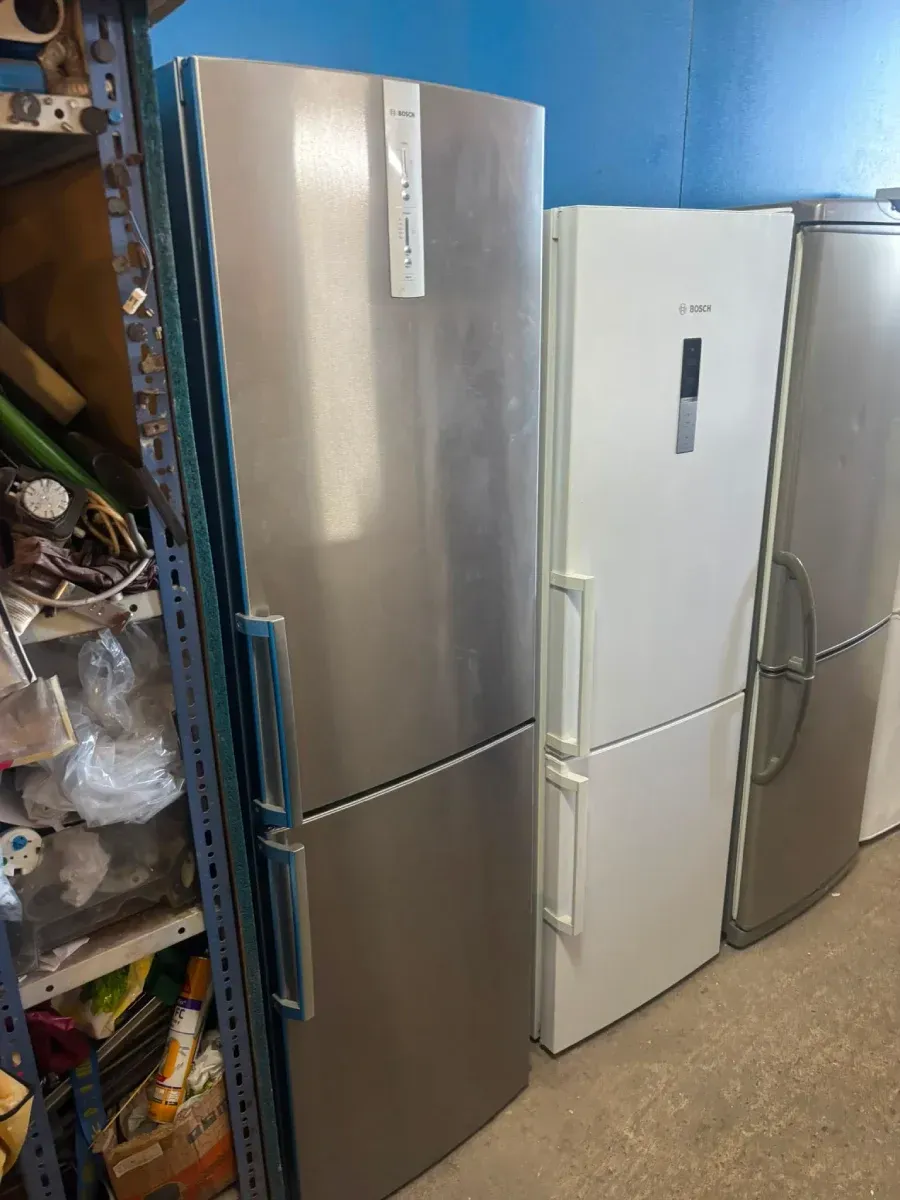 Tres refrigeradores verticales alineados en un pasillo de almacenamiento, incluyendo modelos de acero inoxidable y blancos.