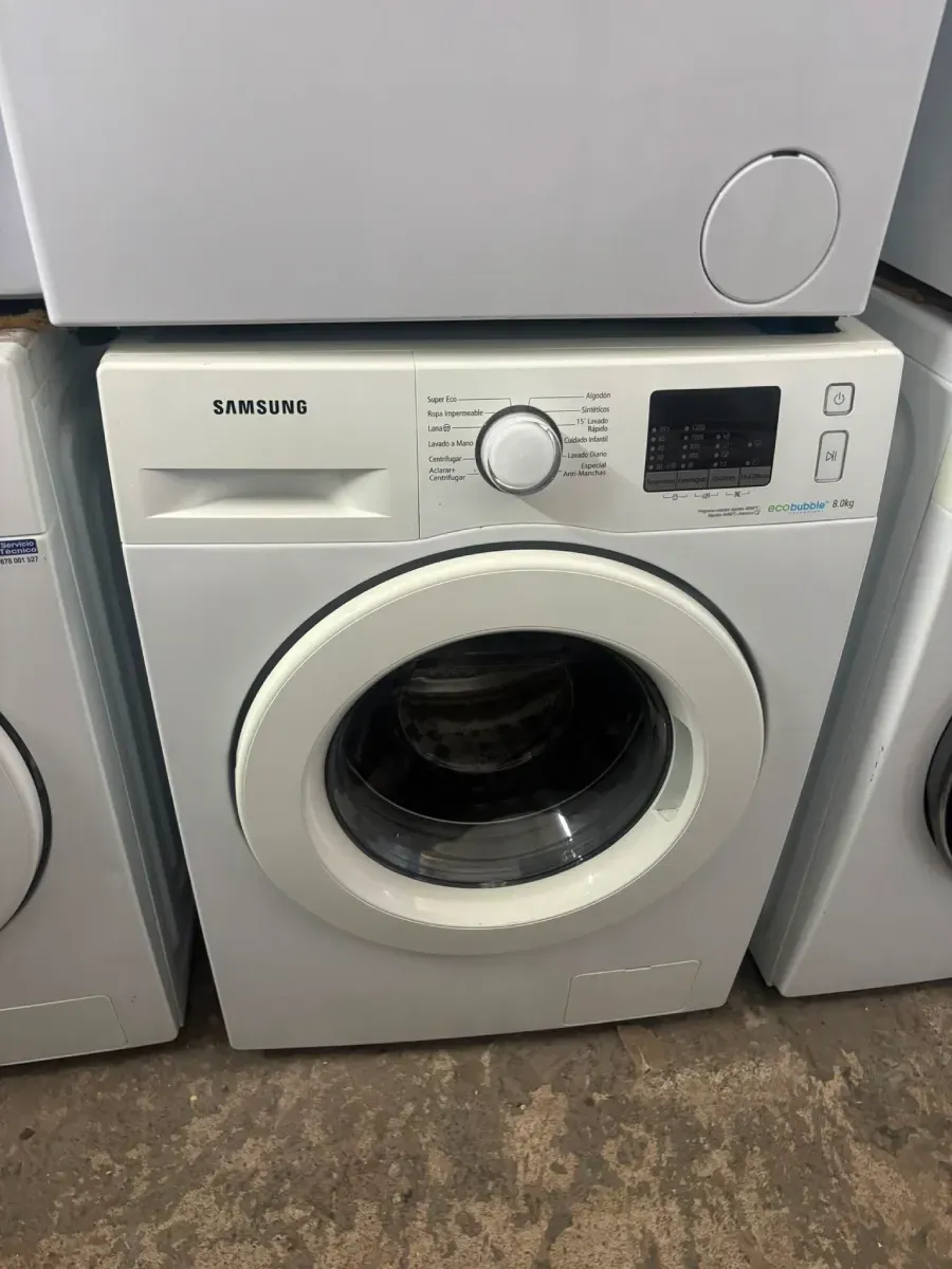 Lavadora Samsung blanca de carga frontal entre electrodomésticos en un cuarto de lavado.