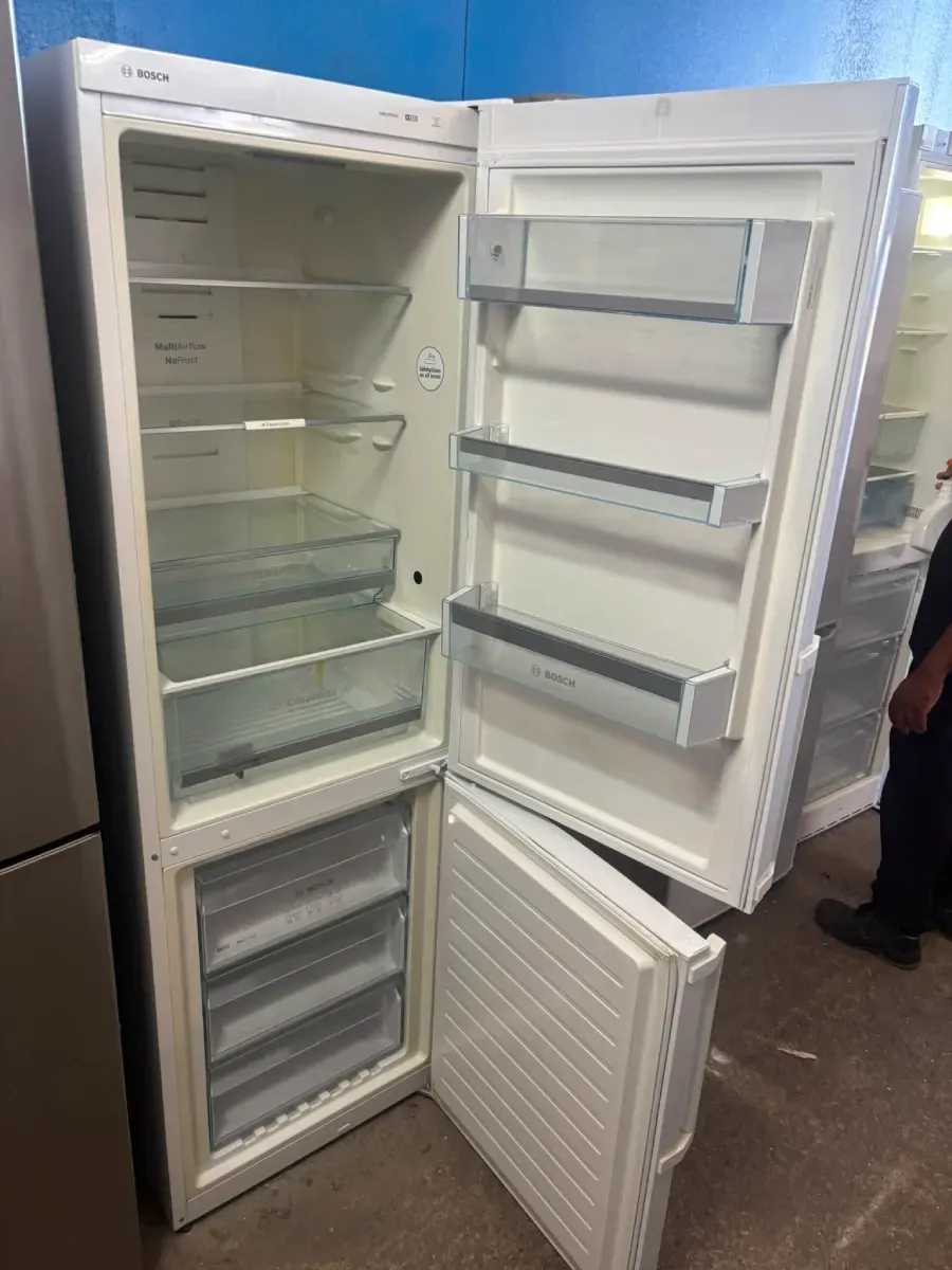Congelador vertical blanco abierto con estantes y cajones, con la puerta abierta, en el pasillo de una tienda.