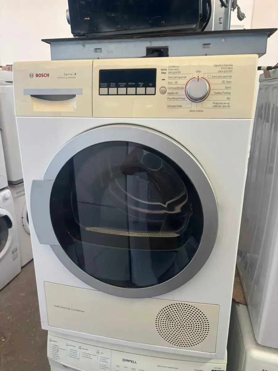 Secadora de carga frontal blanca en un cuarto de lavado con puerta circular negra y panel de control en la parte superior.