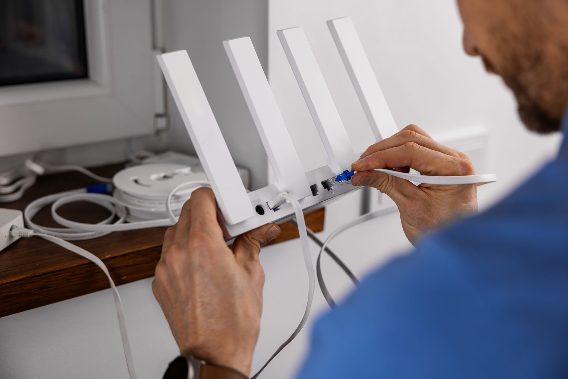 Une personne connecte un câble Ethernet bleu à un routeur Wi-Fi blanc doté de quatre antennes.