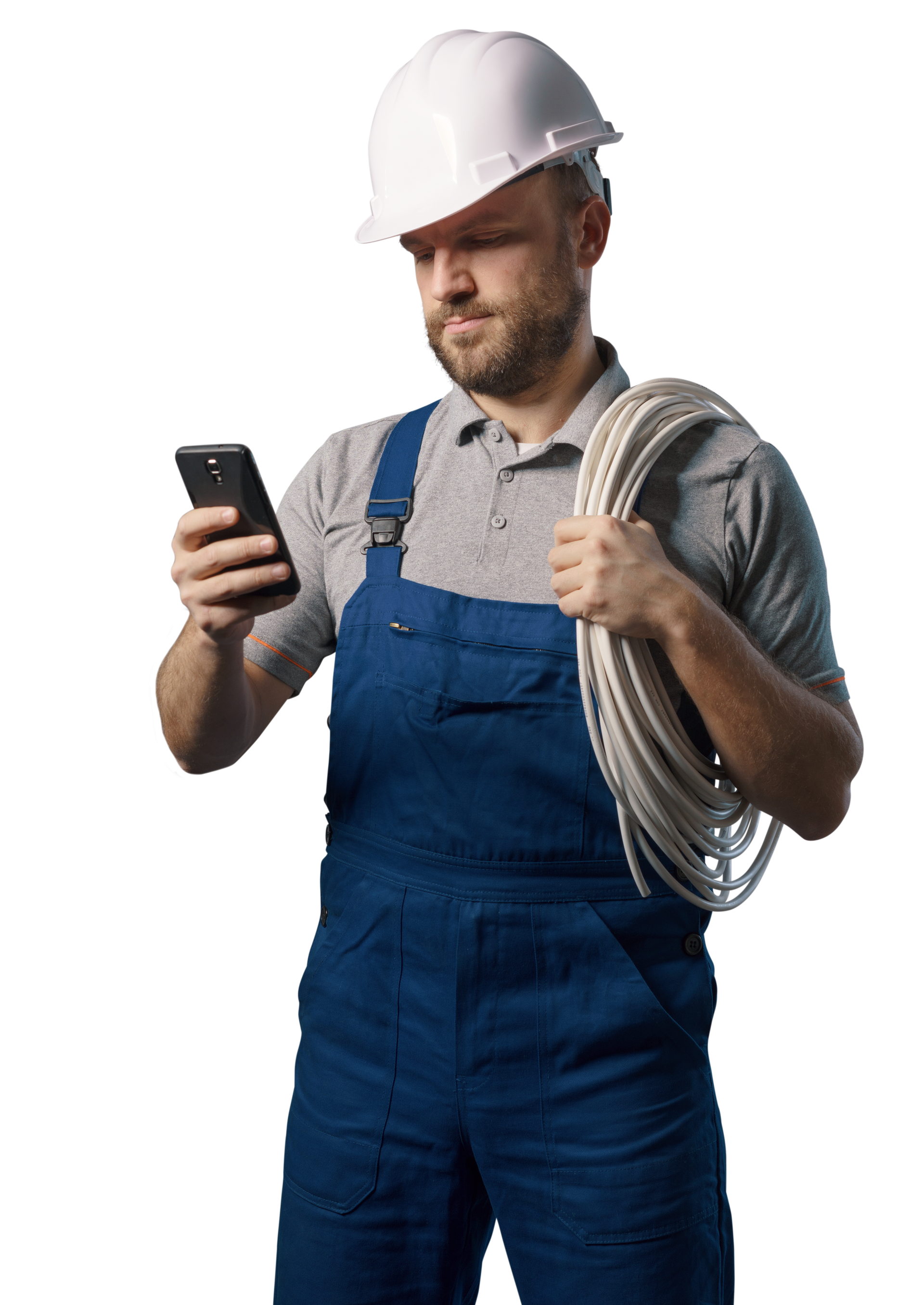 Un ouvrier du bâtiment en salopette bleue avec un casque de chantier regarde un téléphone, tenant une bobine de câble blanc.
