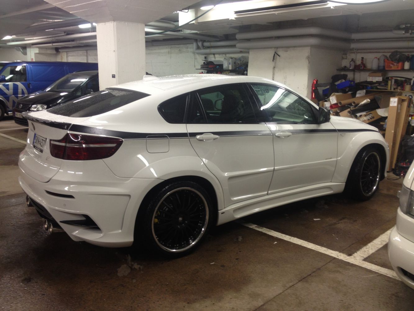 Valkoinen BMW X6 mustilla yksityiskohdilla pysäköitynä autotalliin.