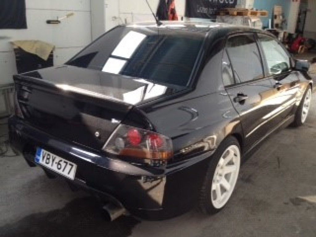 Musta Mitsubishi Lancer Evolution valkoisilla vanteilla pysäköitynä autotalliin.