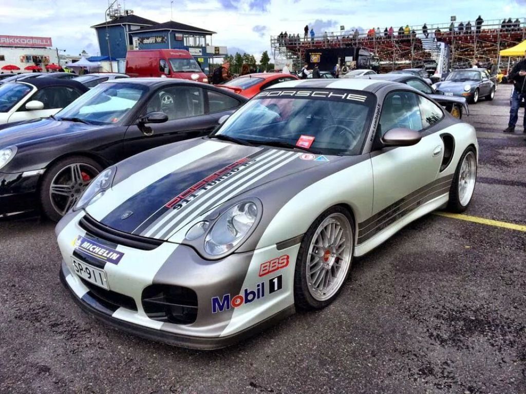 Hopeinen Porsche 911 kilpa-ajoilla ja sponsoritarroilla pysäköitynä autonäyttelyssä.