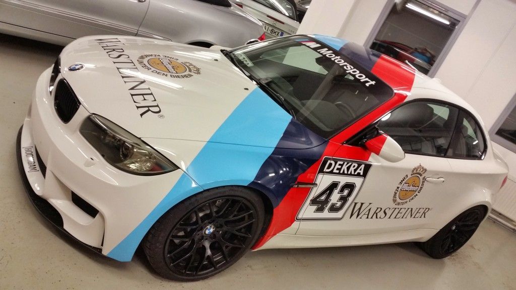 Valkoinen Warsteiner-väreissä, mustilla vanteilla ja numerolla 43 varustettu BMW-urheiluauto autotallissa.