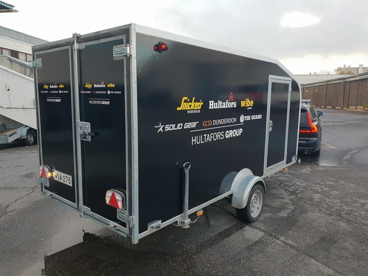 Musta umpinainen perävaunu kytkettynä autoon märällä, päällystetyllä alustalla.