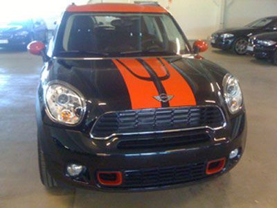 Musta ja oranssi Mini Cooper Countryman kilparaidoilla, pysäköitynä sisätiloissa.