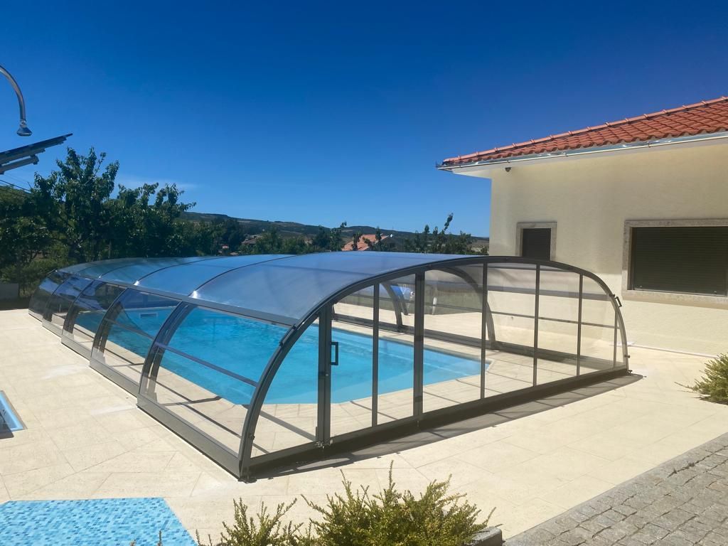 Una piscina con techo transparente y una casa al fondo.