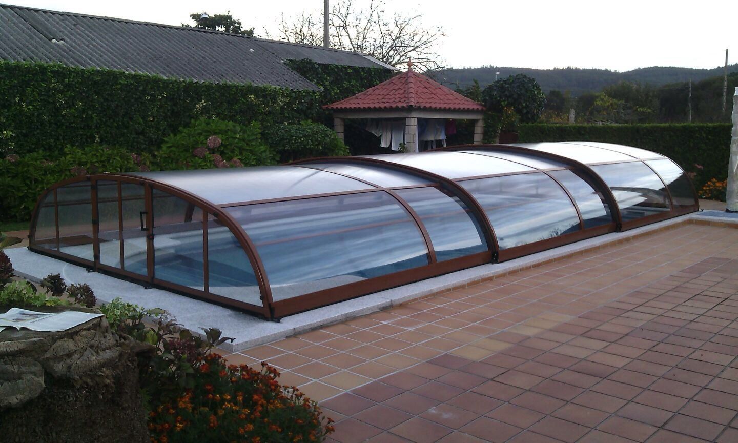 Una piscina con una cubierta encima y un cenador al fondo.