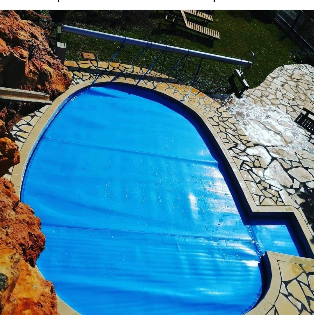 Piscina cubierta de azul con terraza de piedra y jardines a su alrededor.