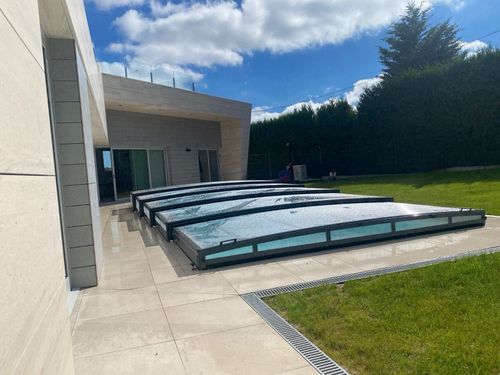 Patio moderno con varios paneles de piscina cubiertos junto a una casa y césped bajo un cielo azul.