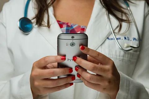 A doctor is holding a cell phone in her hands.