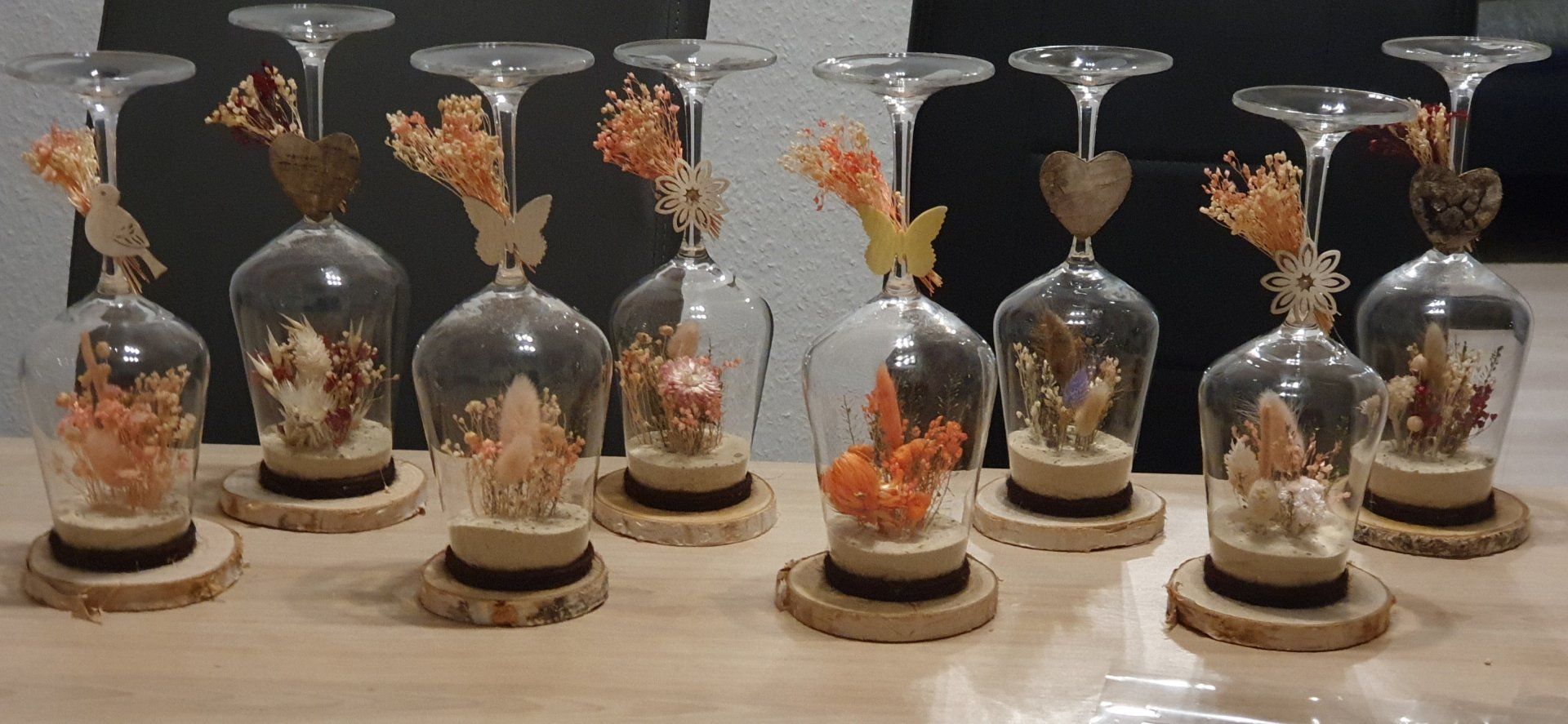 Glasglocken mit Trockenblumenarrangements und kleinen Dekofiguren auf einer Holzoberfläche.