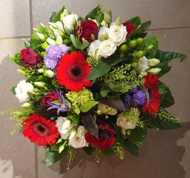 Farbenfroher gemischter Strauss mit roten Gerbera, weissen Rosen, violetten Blüten und grünem Laub