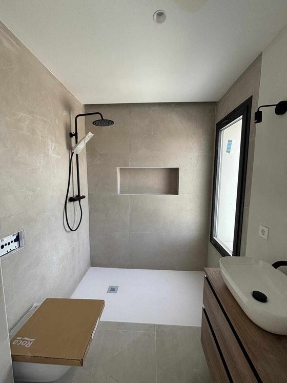 Un fontanero, arrodillado debajo de un fregadero, instala tuberías blancas de PVC con conexiones de cobre en una habitación.