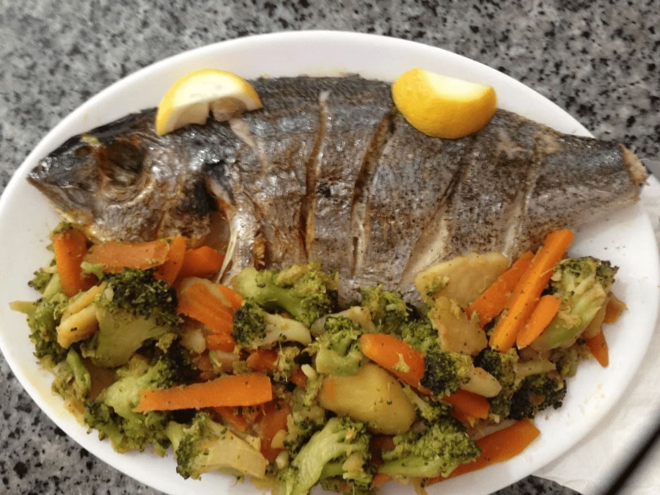 Un plato blanco cubierto con brócoli, zanahorias y un pescado.