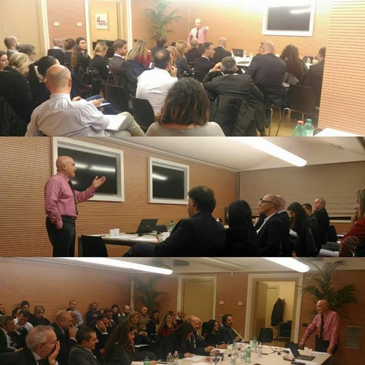 Un uomo con una maglietta rosa sta facendo una presentazione a un gruppo di persone