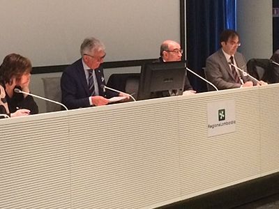 Un gruppo di persone è seduto a un lungo tavolo con dei microfoni