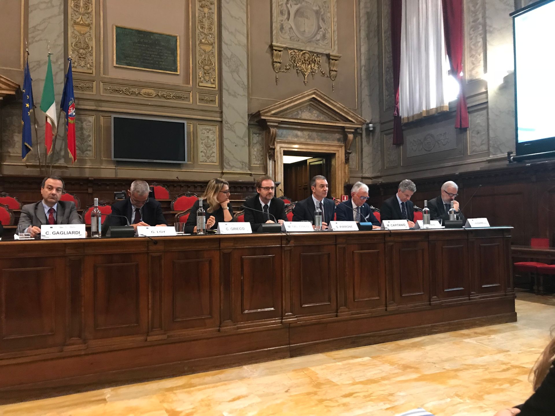 Un gruppo di uomini è seduto attorno a un lungo tavolo di legno in una grande stanza.