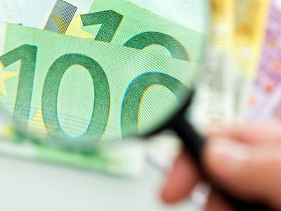 Una persona tiene una lente di ingrandimento sopra una banconota da 100 euro.