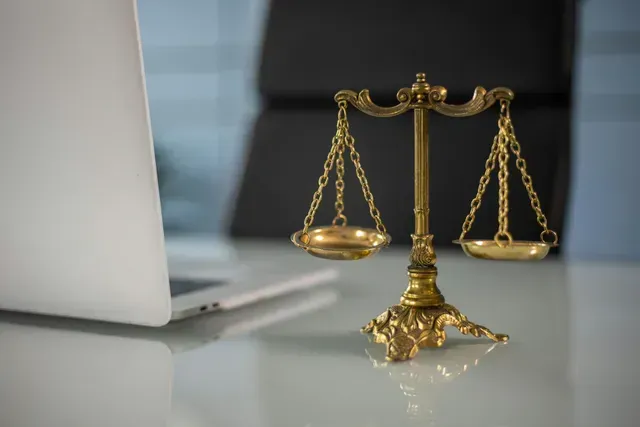 Una bilancia della giustizia è appoggiata su un tavolo accanto a un computer portatile.