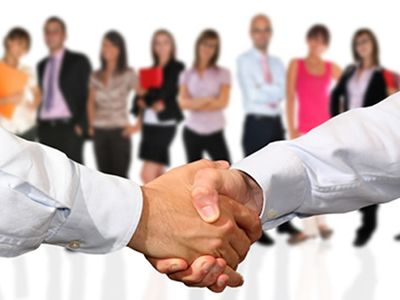 Due persone si stringono la mano davanti a un gruppo di persone.