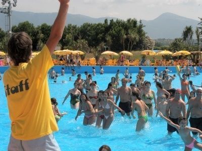 Un uomo con una maglietta gialla da ufficiale è in piedi davanti a una piscina piena di gente