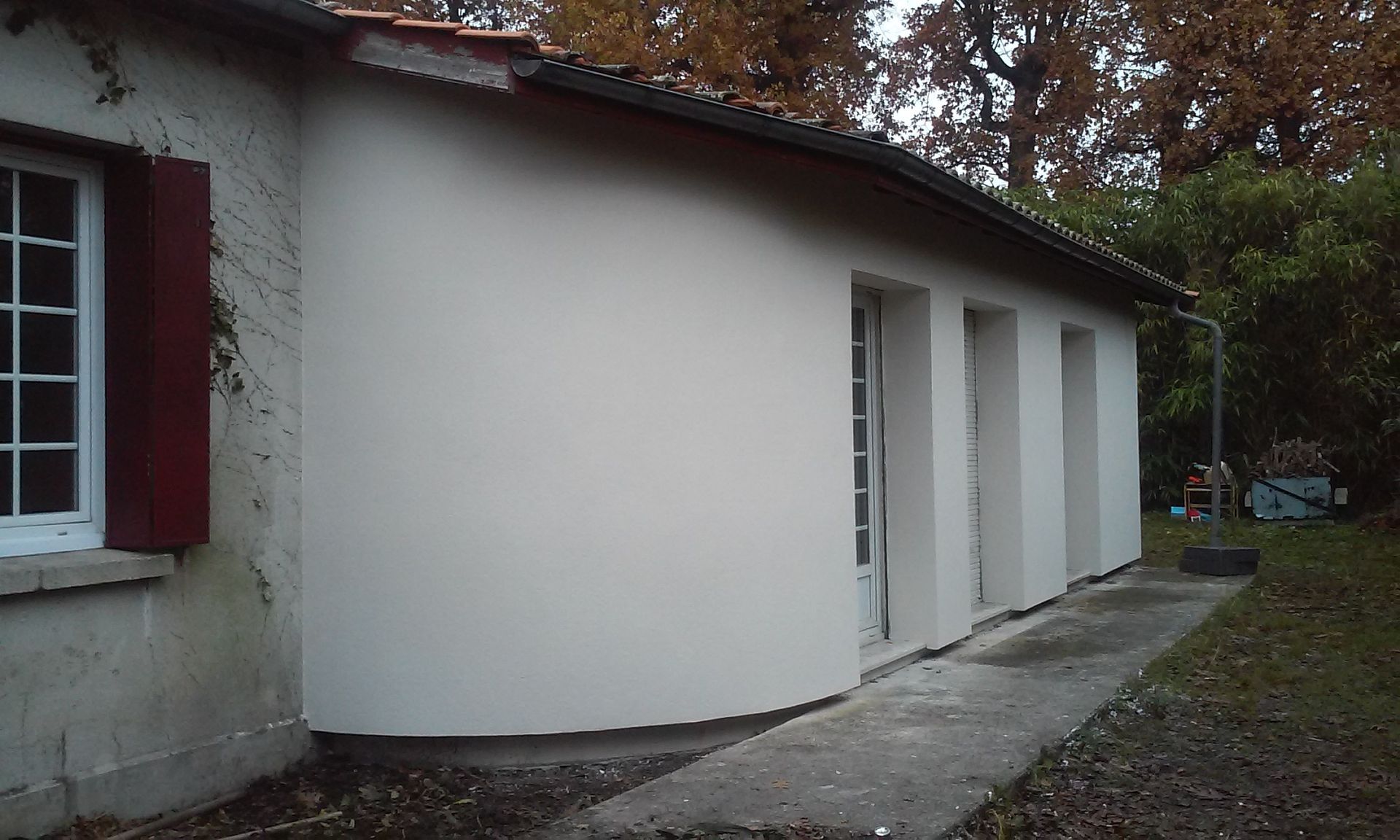 L'extérieur d'une maison blanche de plain-pied, avec une partie de mur arrondie, après ravalement.