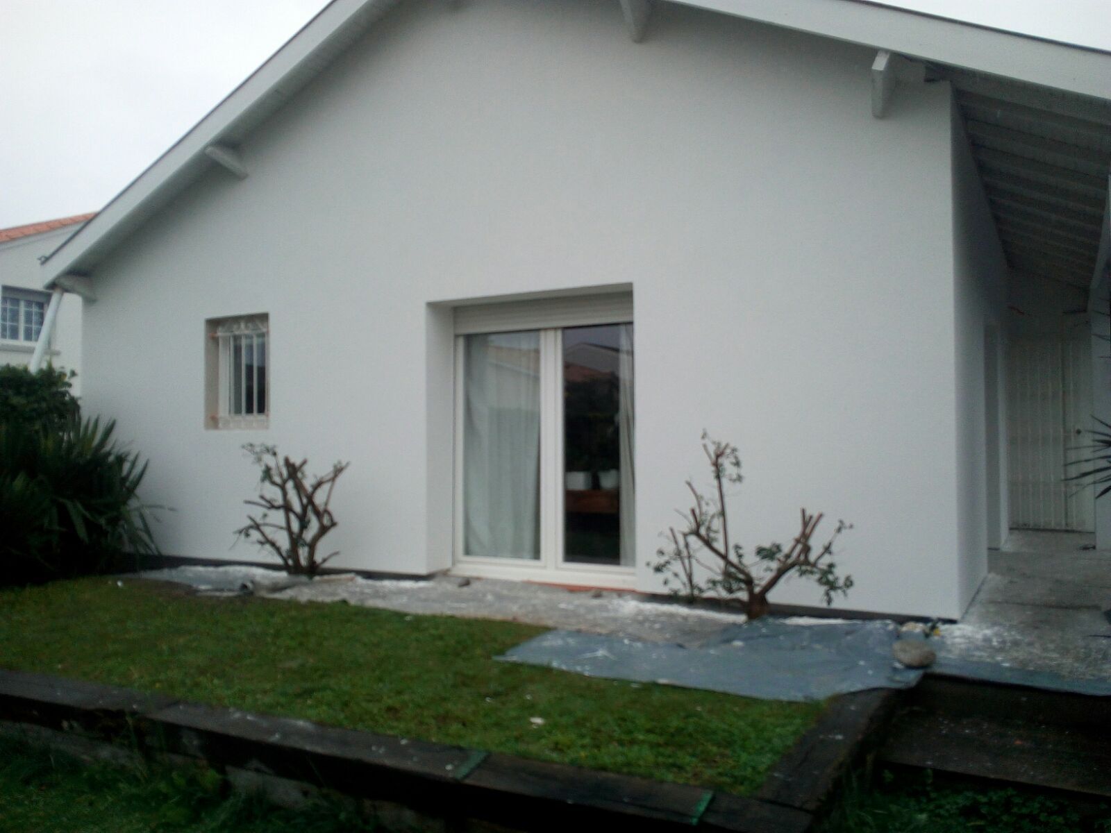 L'extérieur d'une maison blanche présente une porte coulissante vitrée et une petite fenêtre.