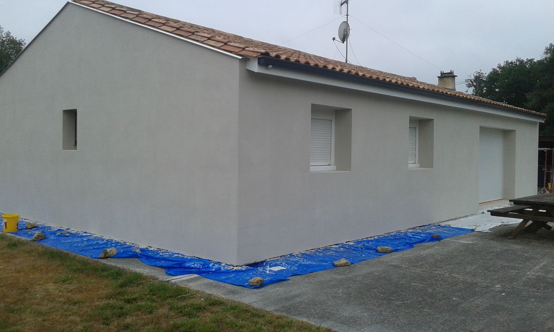 L'extérieur d'une maison de couleur claire est entouré d'une bâche de protection en plastique bleu.