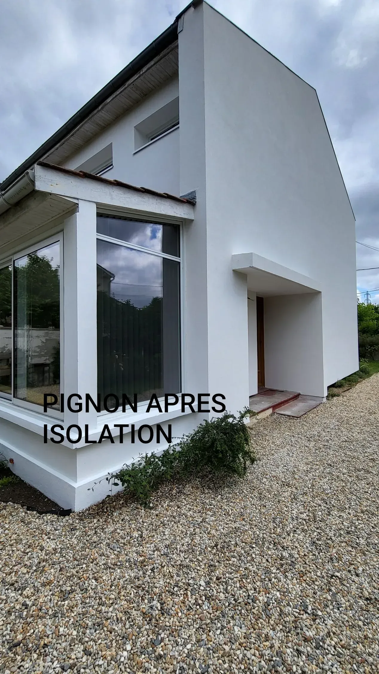 Le pignon d'une maison blanche, avec une véranda vitrée, témoigne du résultat d'une isolation extérieure récente.