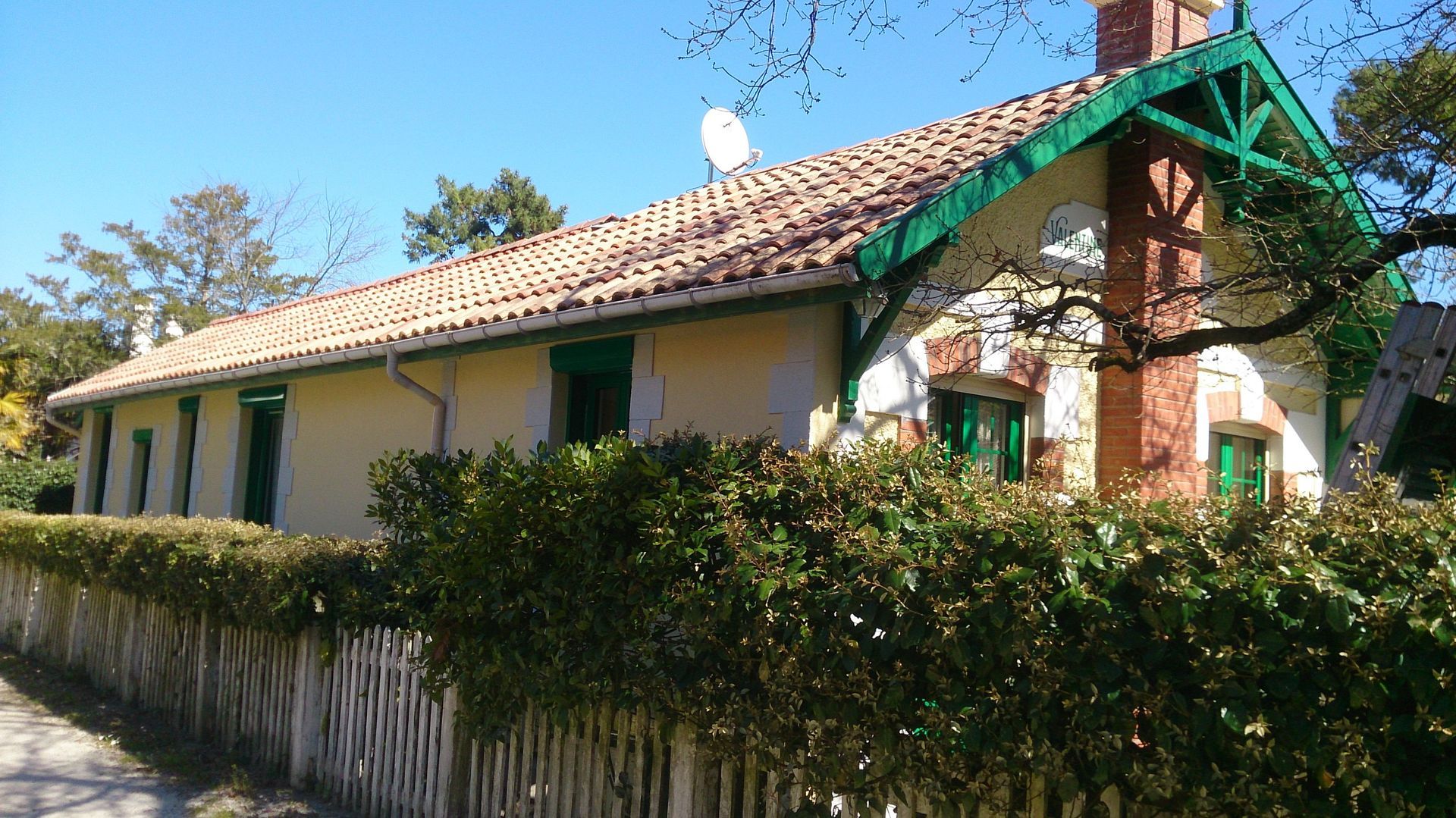 Une maison de plain-pied avec un toit de tuiles en terre cuite, des murs jaunes et des boiseries vertes.