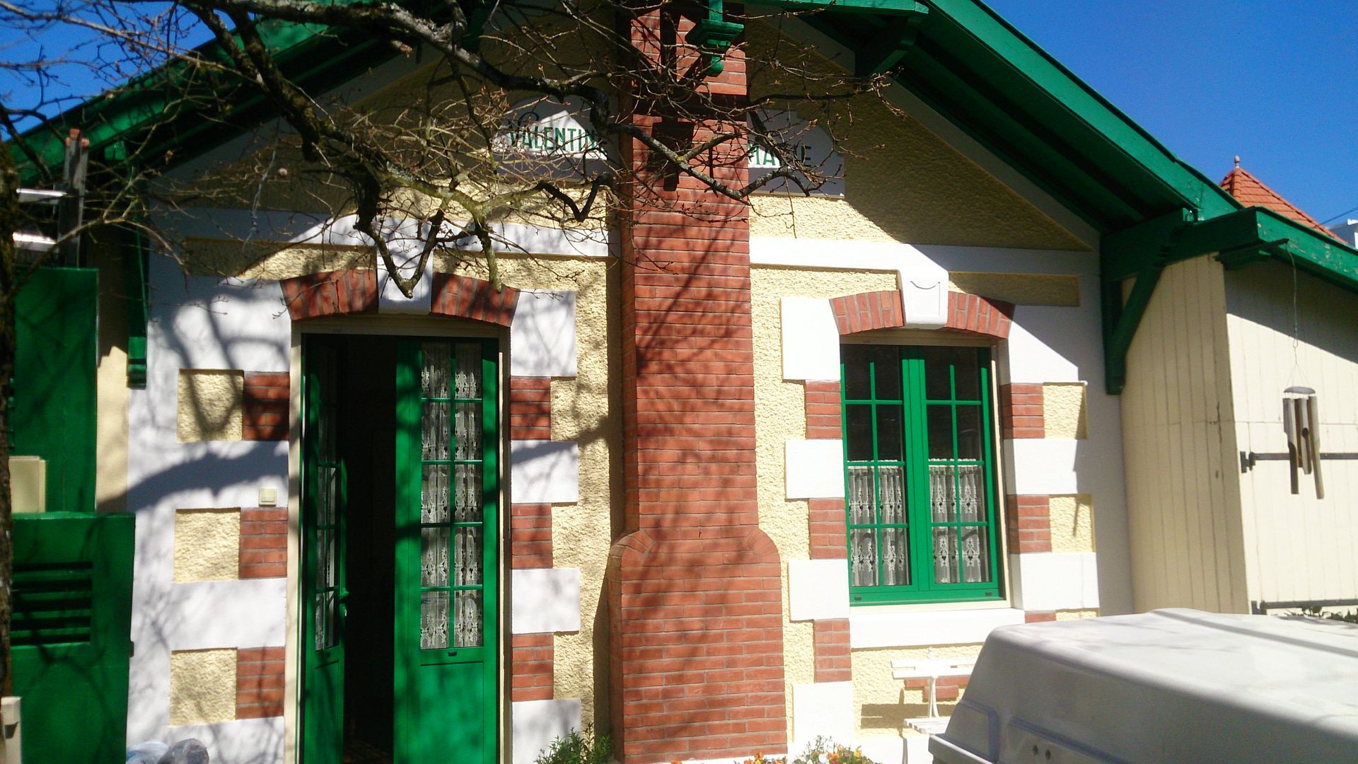 Une maison avec des menuiseries vertes, des murs couleur crème et des ornements en briques.