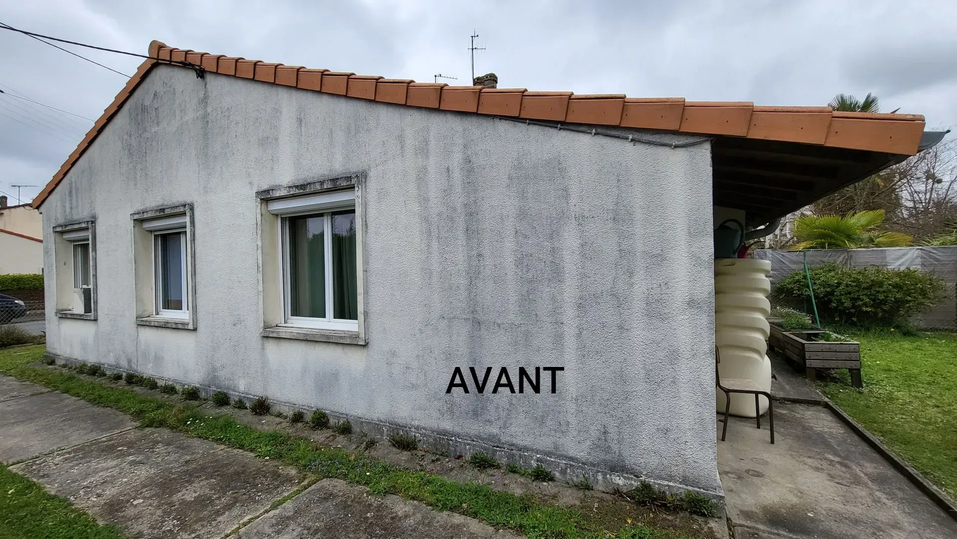 Vue latérale d'une maison à la façade défraîchie, avec trois fenêtres et un toit de tuiles en terre cuite.