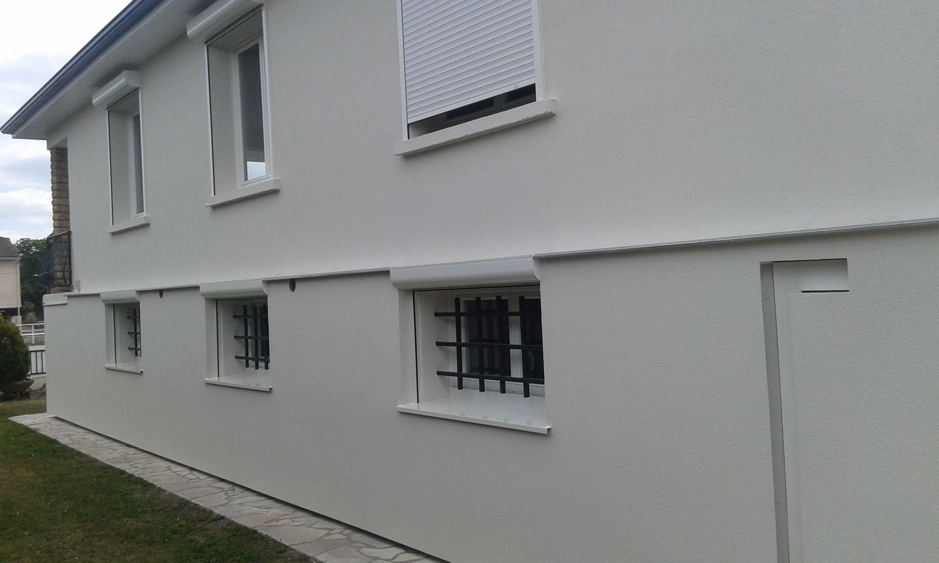 L'extérieur d'une maison blanche à deux étages présente des fenêtres avec barreaux de sécurité au rez-de-chaussée.