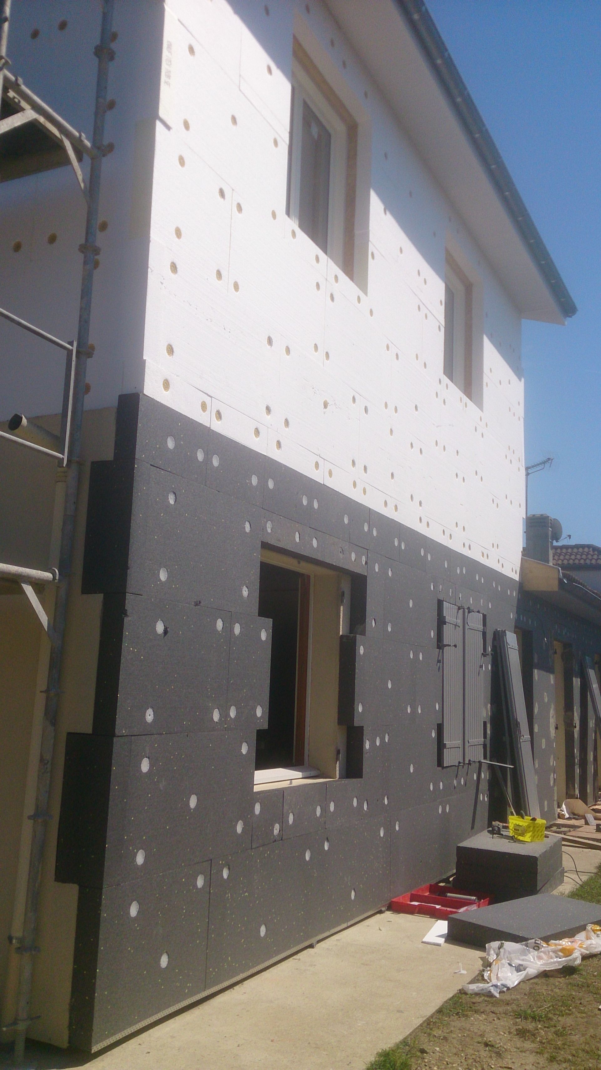 L'extérieur d'une maison en cours de rénovation, avec des panneaux d'isolation thermique blancs et noirs fixés aux murs.