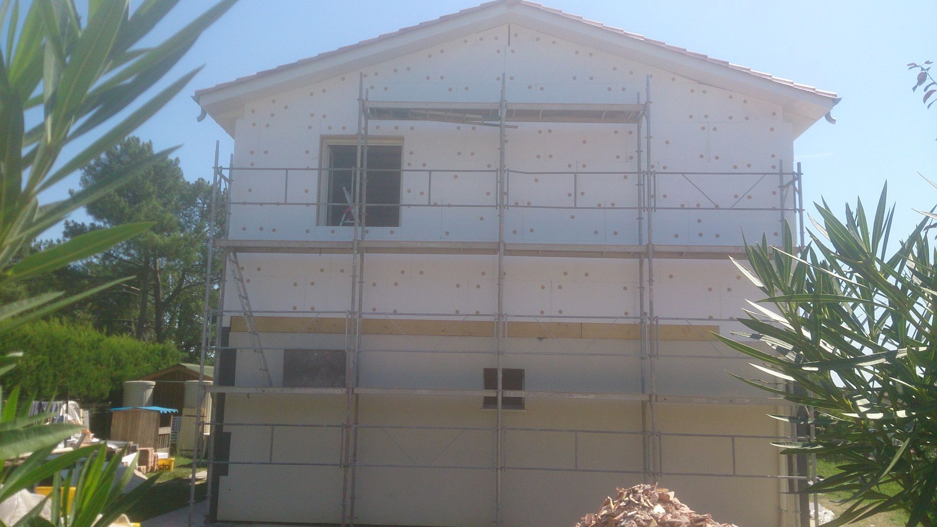 Façade d'une maison en rénovation, recouverte de panneaux isolants blancs, avec des échafaudages devant.