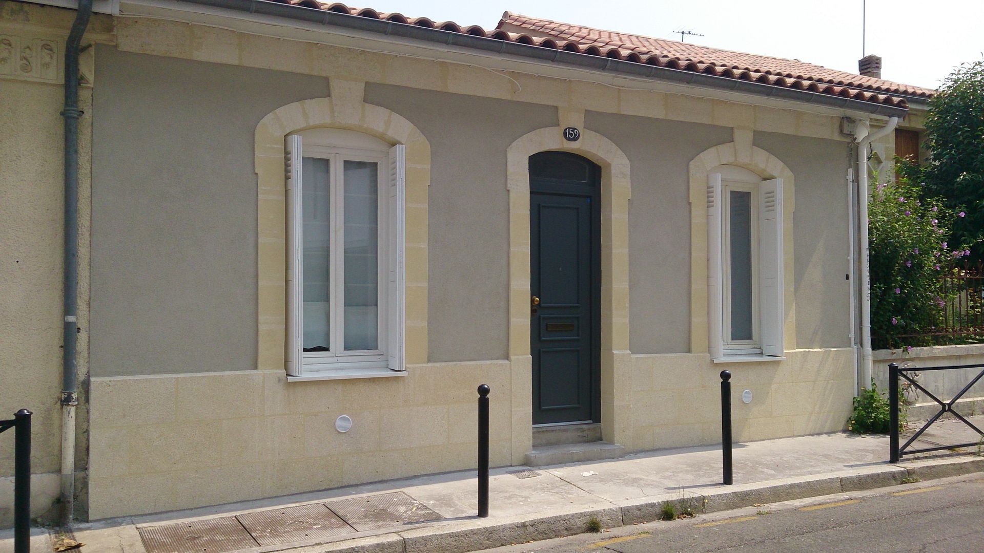 Une maison de plain-pied gris clair avec des ornements en pierre couleur crème, une porte sombre et deux fenêtres.