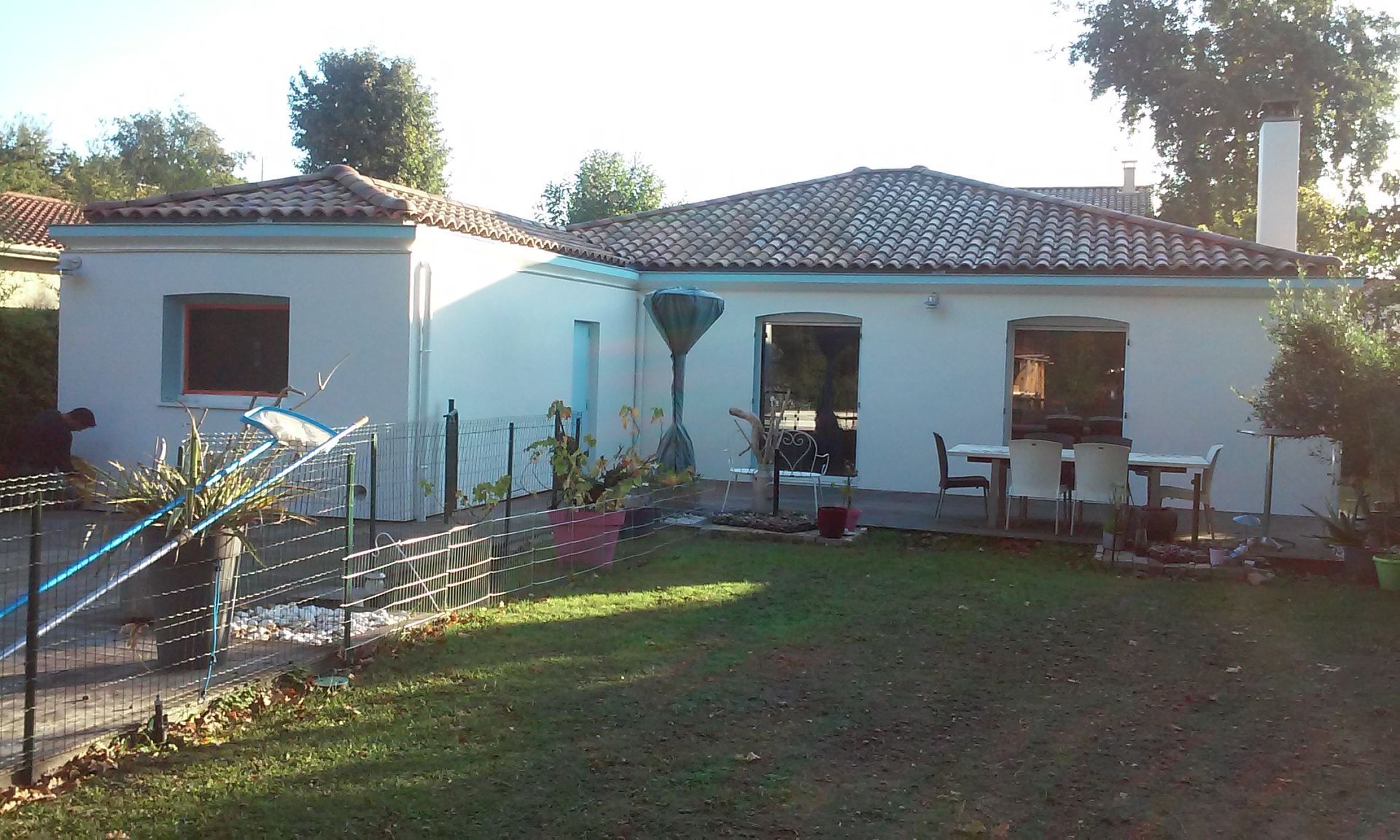 Une maison blanche de plain-pied en forme de L, avec un toit de tuiles rouges et un ensemble de mobilier de patio extérieur.