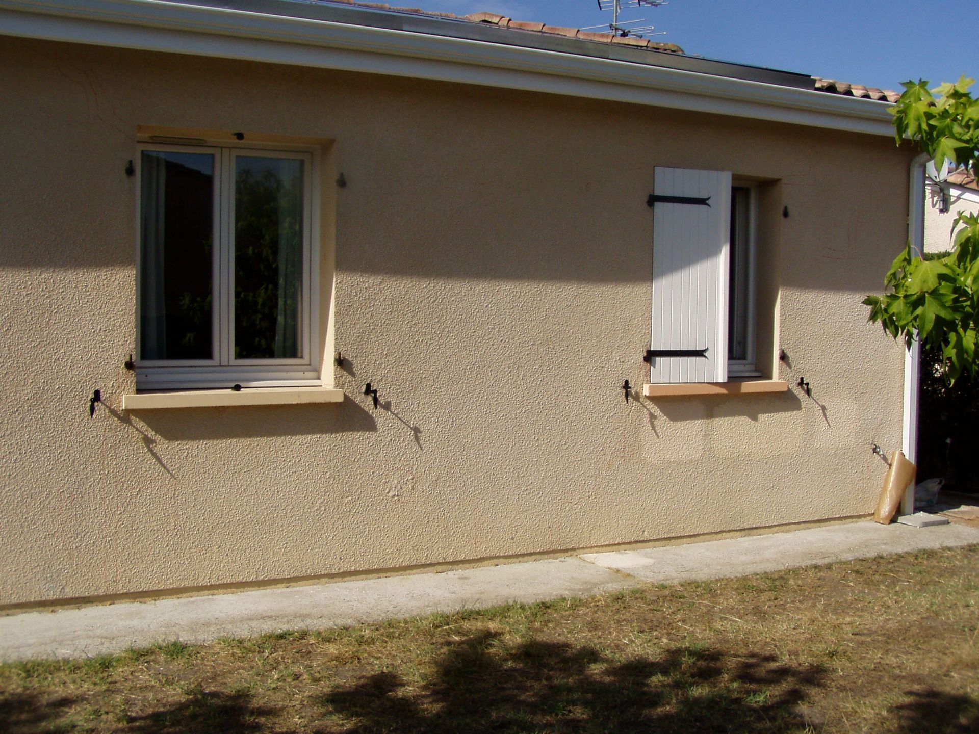 Un mur extérieur beige avec deux fenêtres, après ravalement de façade.